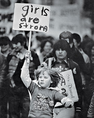 Girl holding sign that reads: Girls Are Strong